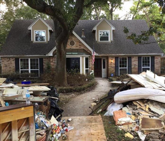 Brick two story home with trees surrounding and rubble outside after hurricane passed