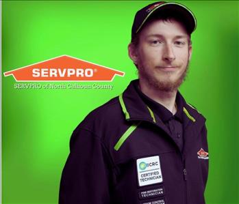 White male brown hair in black jacket with white patch and green trim. Standing against green wall with SERVPRO logo.